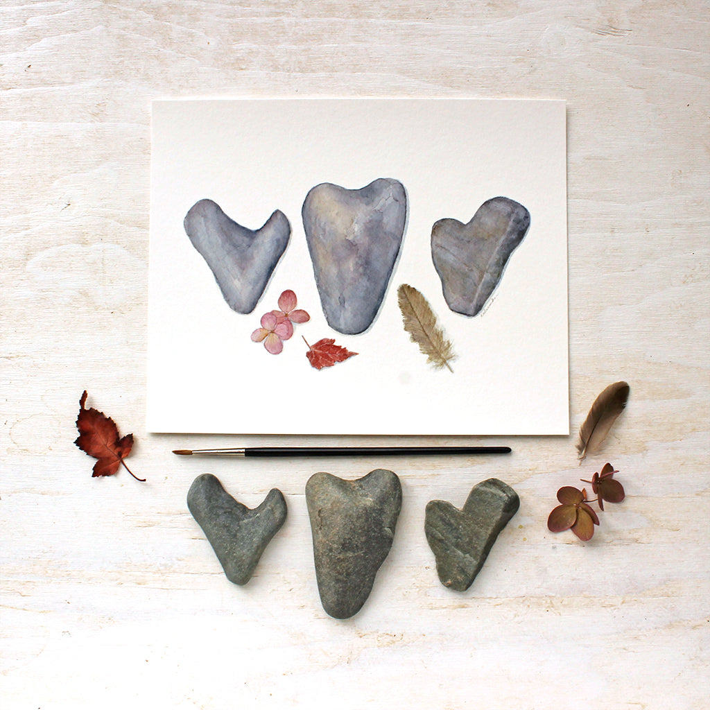 Art print of a lovely watercolor painting depicting three heart shaped rocks, a sparrow feather, leaf and hydrangea blossom. Artist Kathleen Maunder.