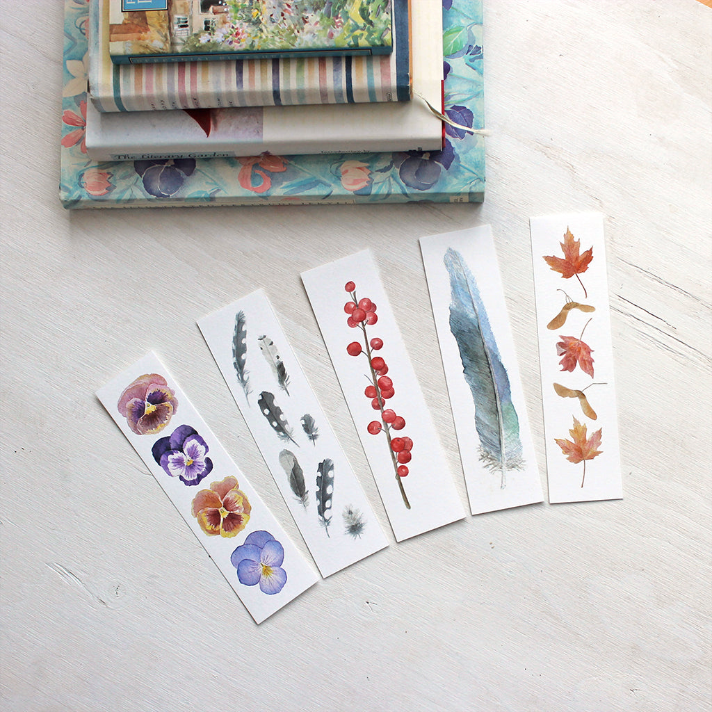 Set of five watercolor bookmarks by Kathleen Maunder. Set includes pansies, woodpecker feathers, winterberries, blue feather and maple leaves.