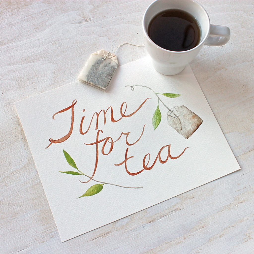 An art print featuring a lovely watercolor painting with the hand-lettered words 'Time for Tea', a tea bag and a sprig of a tea plant. Artist Kathleen Maunder.