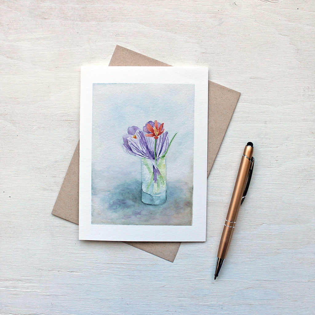A note card featuring a watercolour painting of a tiny vase of spring flowers: two crocuses and a botanical tulip. Artist Kathleen Maunder.