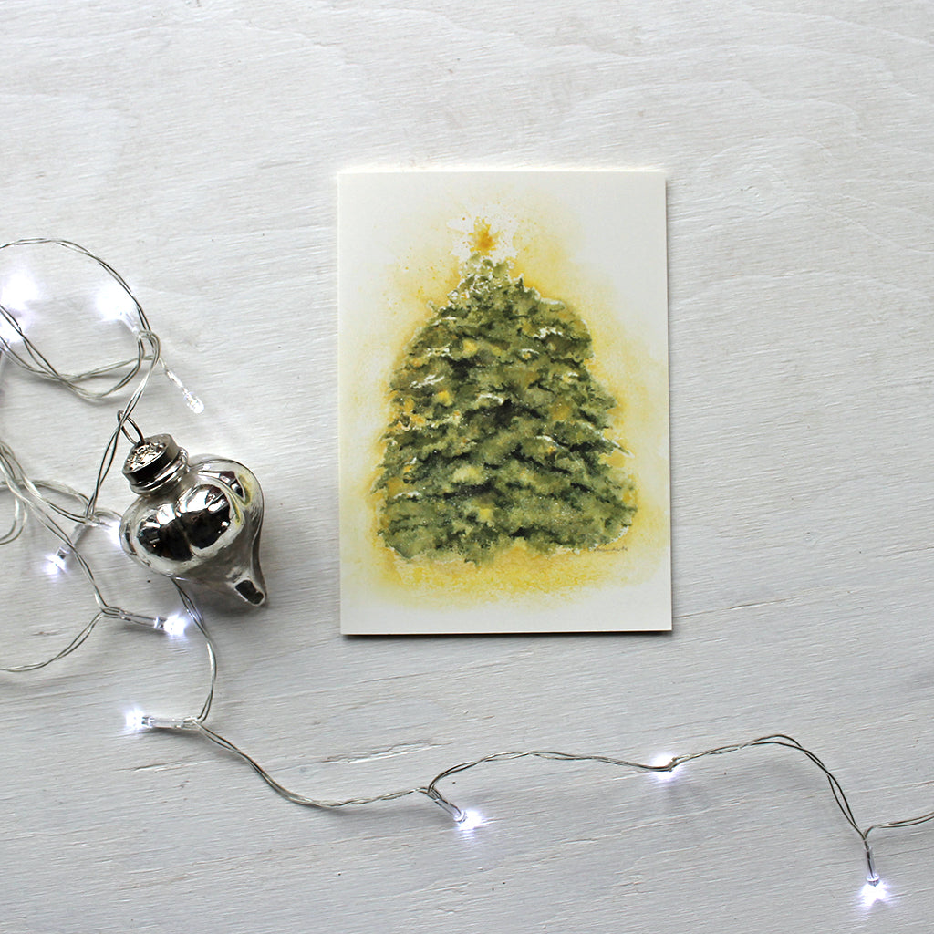 A holiday card featuring a glowing holiday tree covered in snow and sparkles and topped with a starry light. Artist Kathleen Maunder
