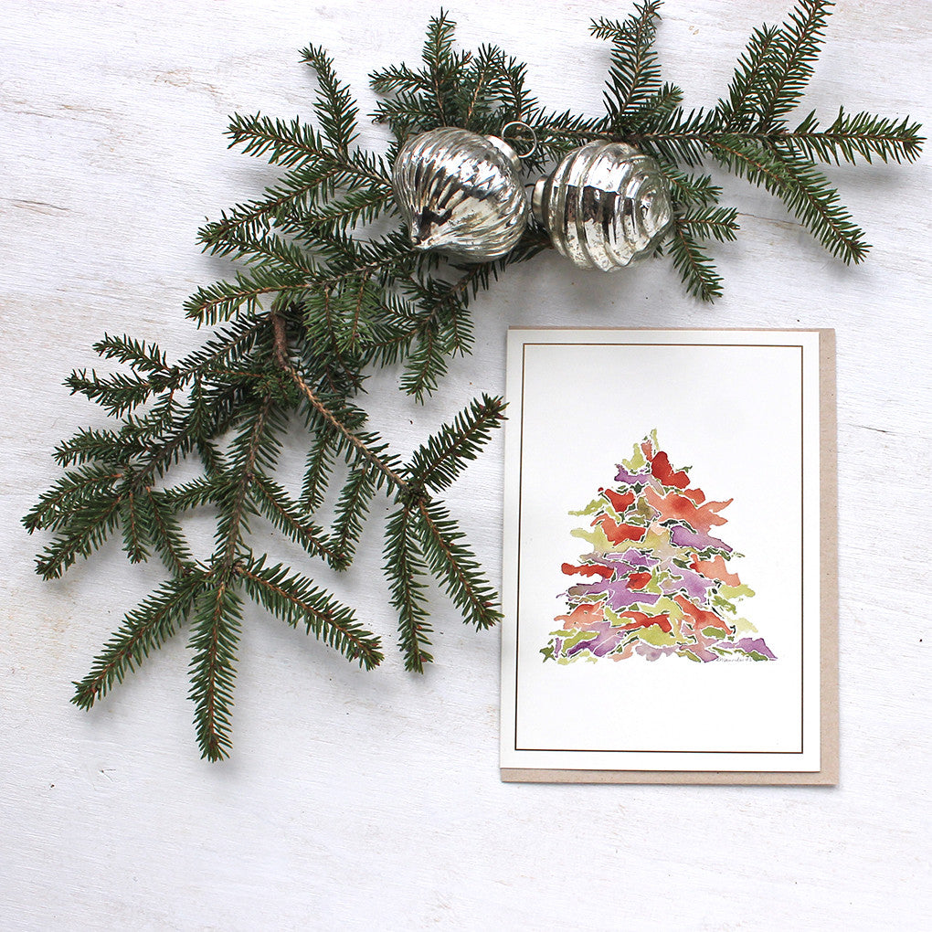 A holiday card featuring a multi-coloured Christmas tree painted in watercolor. Festive tones of red, green and purple. Artist Kathleen Maunder