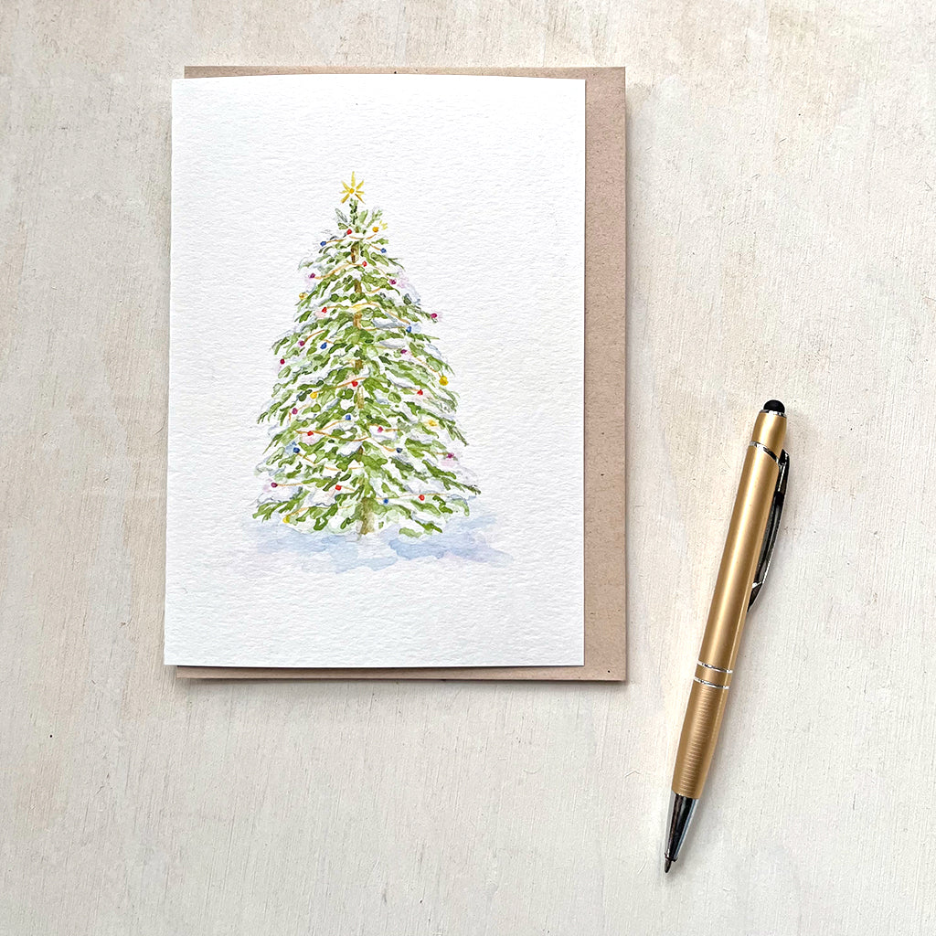 A beautiful holiday card featuring a watercolor painting of a Christmas tree with snow-covered branches and  colorful lights. Artist Kathleen Maunder.