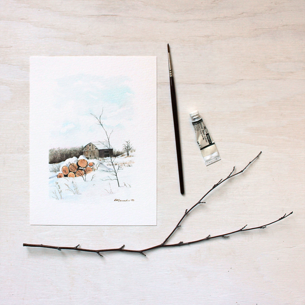 An art print of a watercolor painting of a rural winter scene including a barn and stack of logs. Artist Kathleen Maunder.