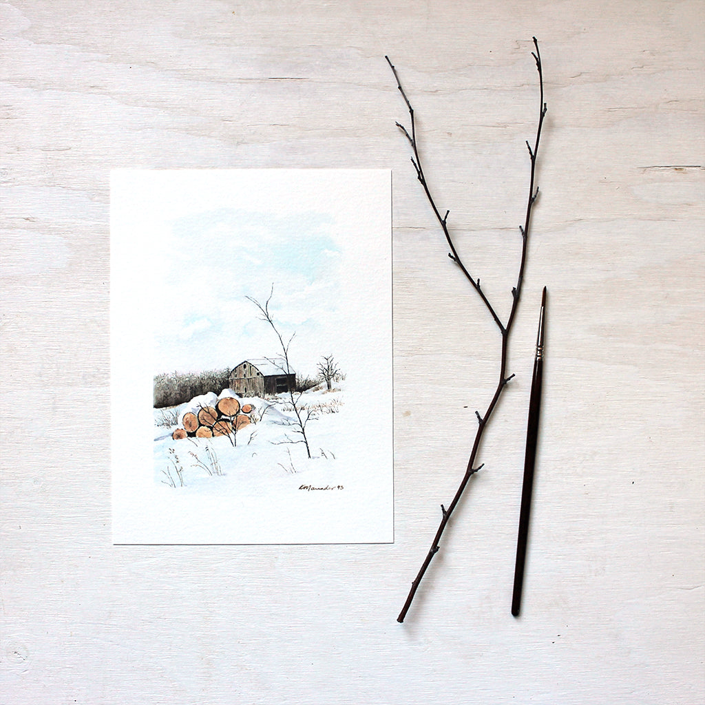 An art print of a watercolor painting of a rural winter scene including a barn and stack of logs. Artist Kathleen Maunder.
