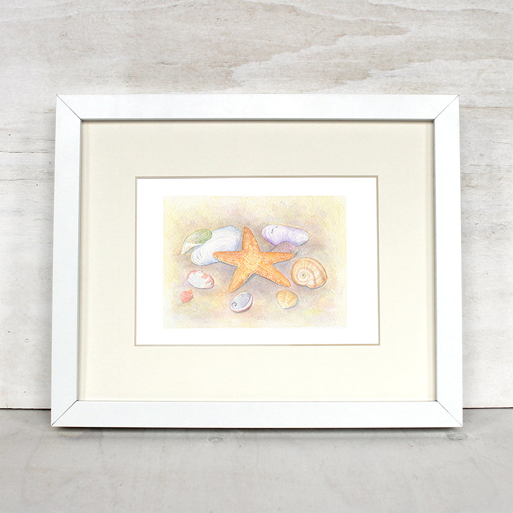 Art print depicting a watercolor painting of a collection of sea shells and a starfish. Shown framed. Artist Kathleen Maunder.