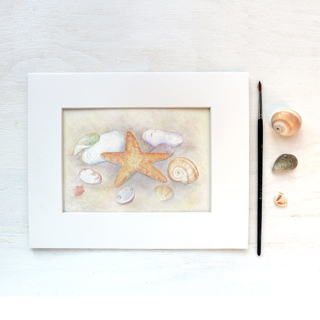 Art print depicting a watercolor painting of a collection of sea shells and a starfish. Shown matted.  Artist Kathleen Maunder.