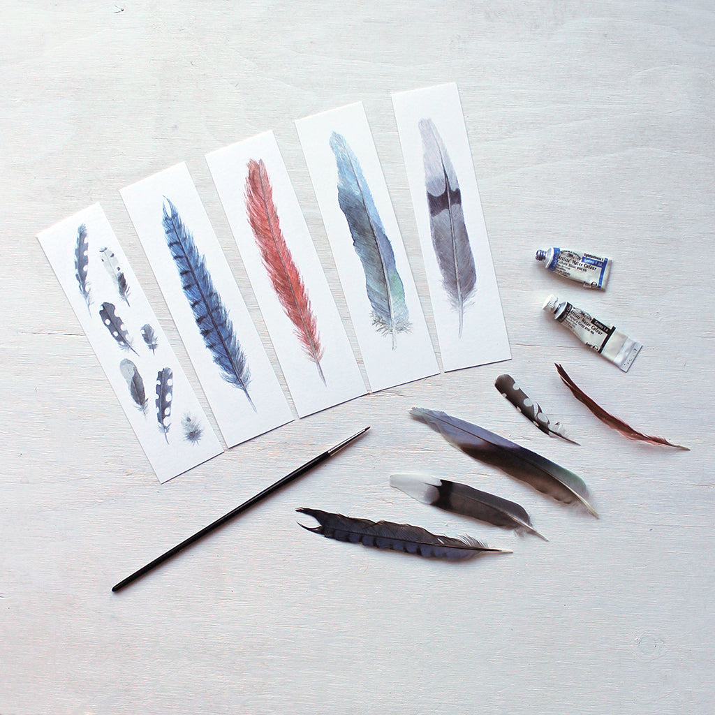 Set of five bookmarks featuring watercolor paintings of bird feathers: woodpecker, blue jay, cardinal, parrot and mourning dove.