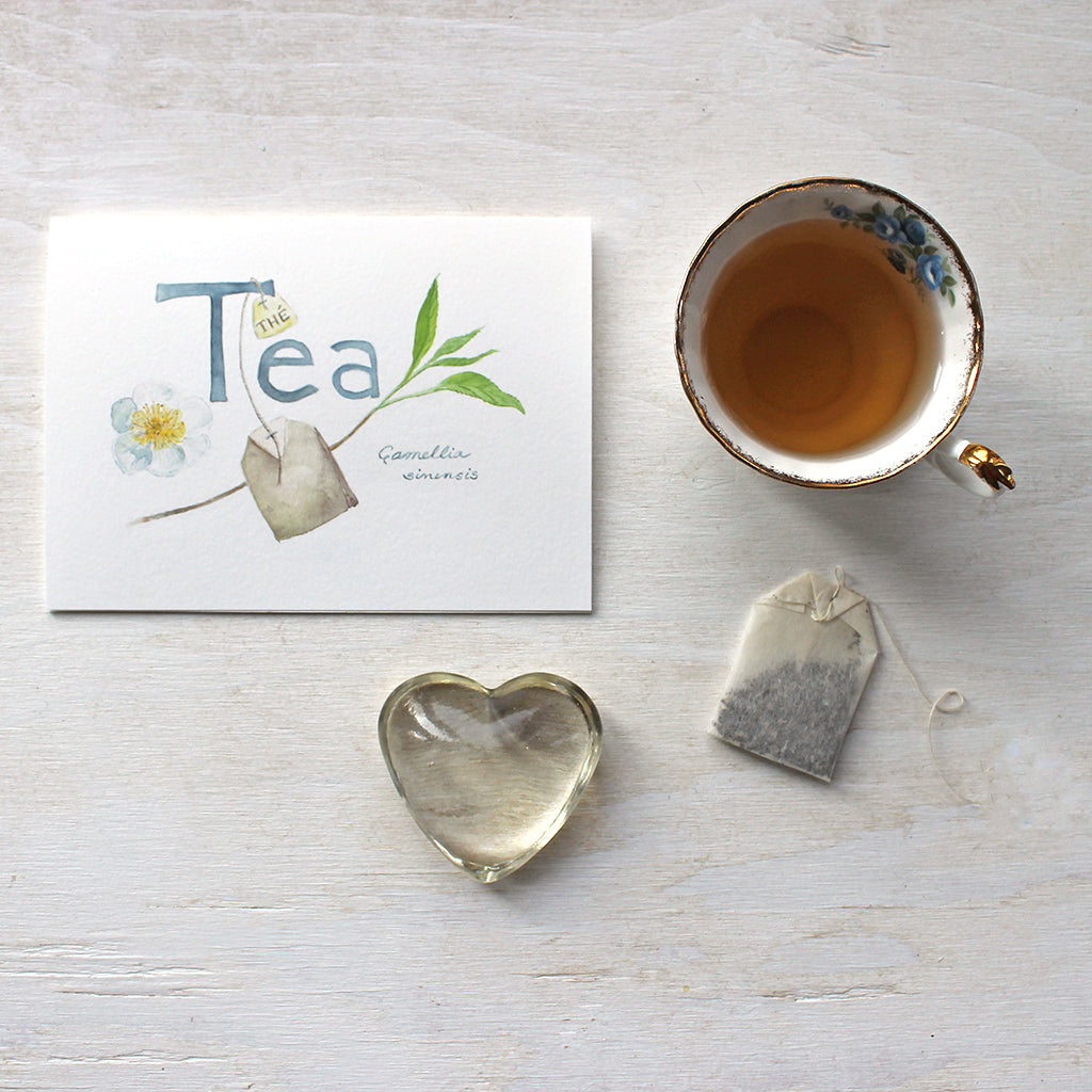 Botanical tea note card by watercolour artist Kathleen Maunder. The image includes a camellia sinensis flower, tea leaves, a tea bag and the hand lettered word 'Tea'.
