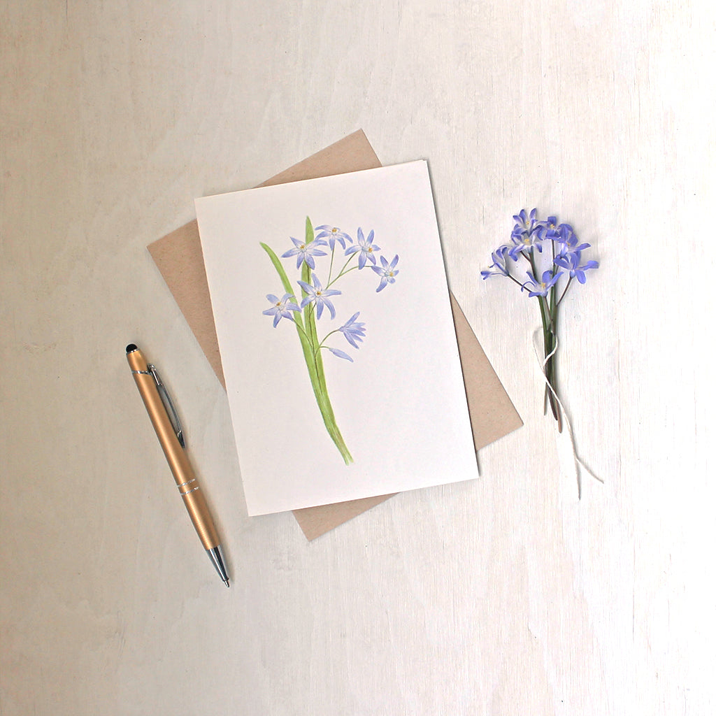 A note card featuring a watercolor painting of blue chionodoxa (glory of the snow) by artist Kathleen Maunder.