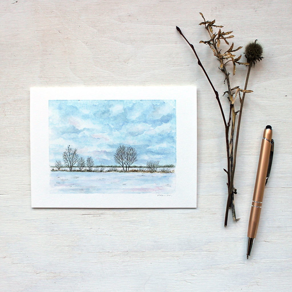 Note card featuring a watercolour painting of a snowy field, a line of trees and a cloudy sky. Artist Kathleen Maunder.