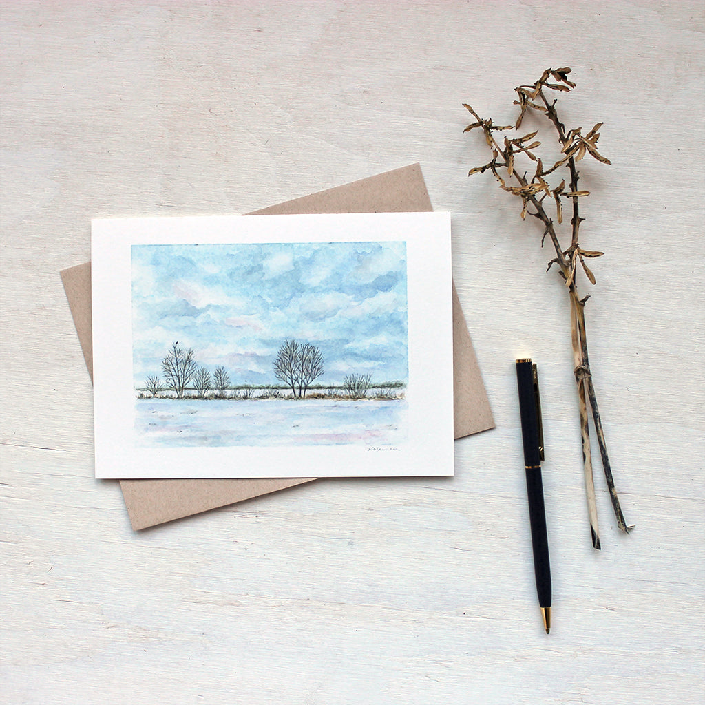 Note card featuring a watercolor painting of a snowy field, a line of trees and a tiny bird. Artist Kathleen Maunder.