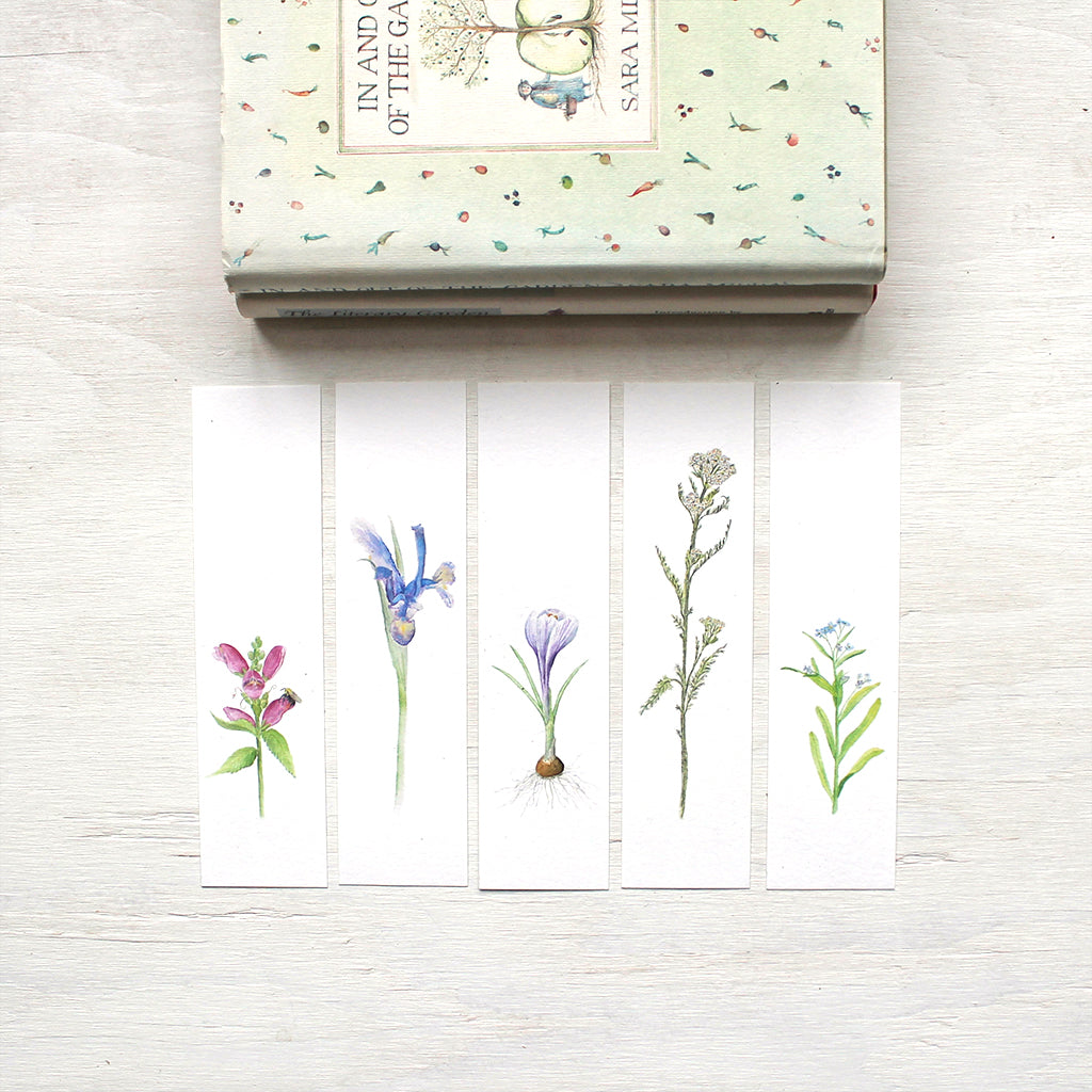 Five floral bookmarks featuring watercolor paintings of turtlehead, an iris, a purple crocus bulb, yarrow and forget me nots. Artist Kathleen Maunder