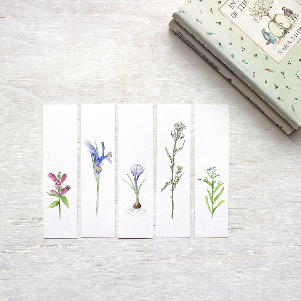 Five botanical bookmarks featuring watercolor paintings of turtlehead, an iris, a purple crocus bulb, yarrow and forget me nots. Artist Kathleen Maunder