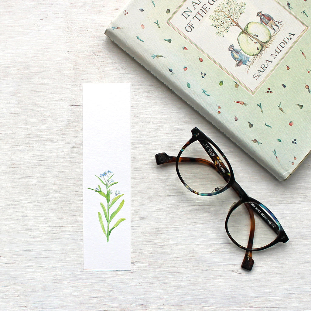 A lovely paper bookmark featuring a watercolour painting of a stem of blue forget me nots. Artist Kathleen Maunder.