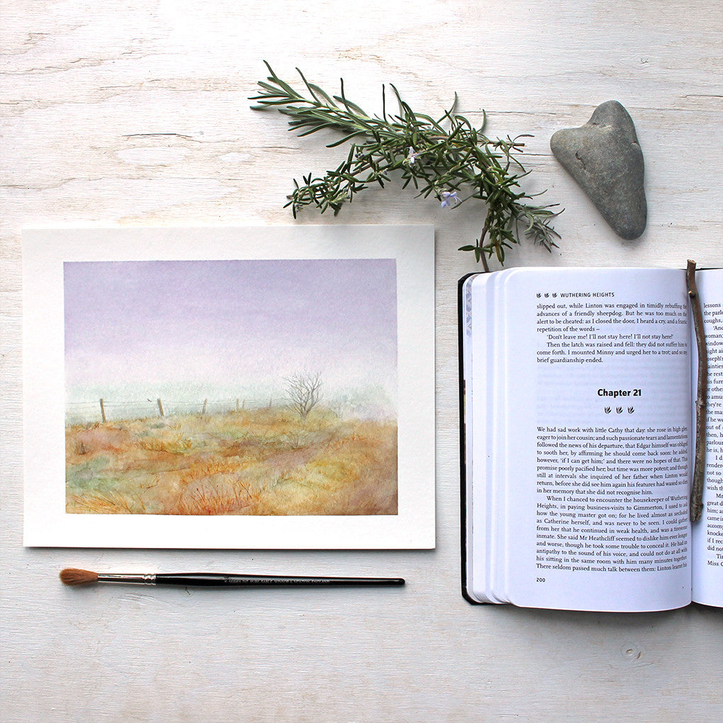 An art print of a delicate moody watercolor painting of misty Haworth Moor where the Brontë sisters used to walk. Artist Kathleen Maunder of Trowel and Paintbrush. (Copy of Wuthering Heights, a heart-shaped rock and blooming lavender also visible.)