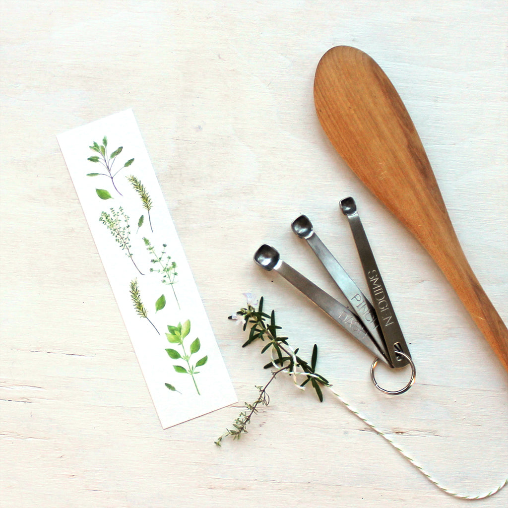 A paper bookmark featuring herbs painted in watercolor by artist Kathleen Maunder. Featuring sage, thyme, rosemary, summer savory and basil.