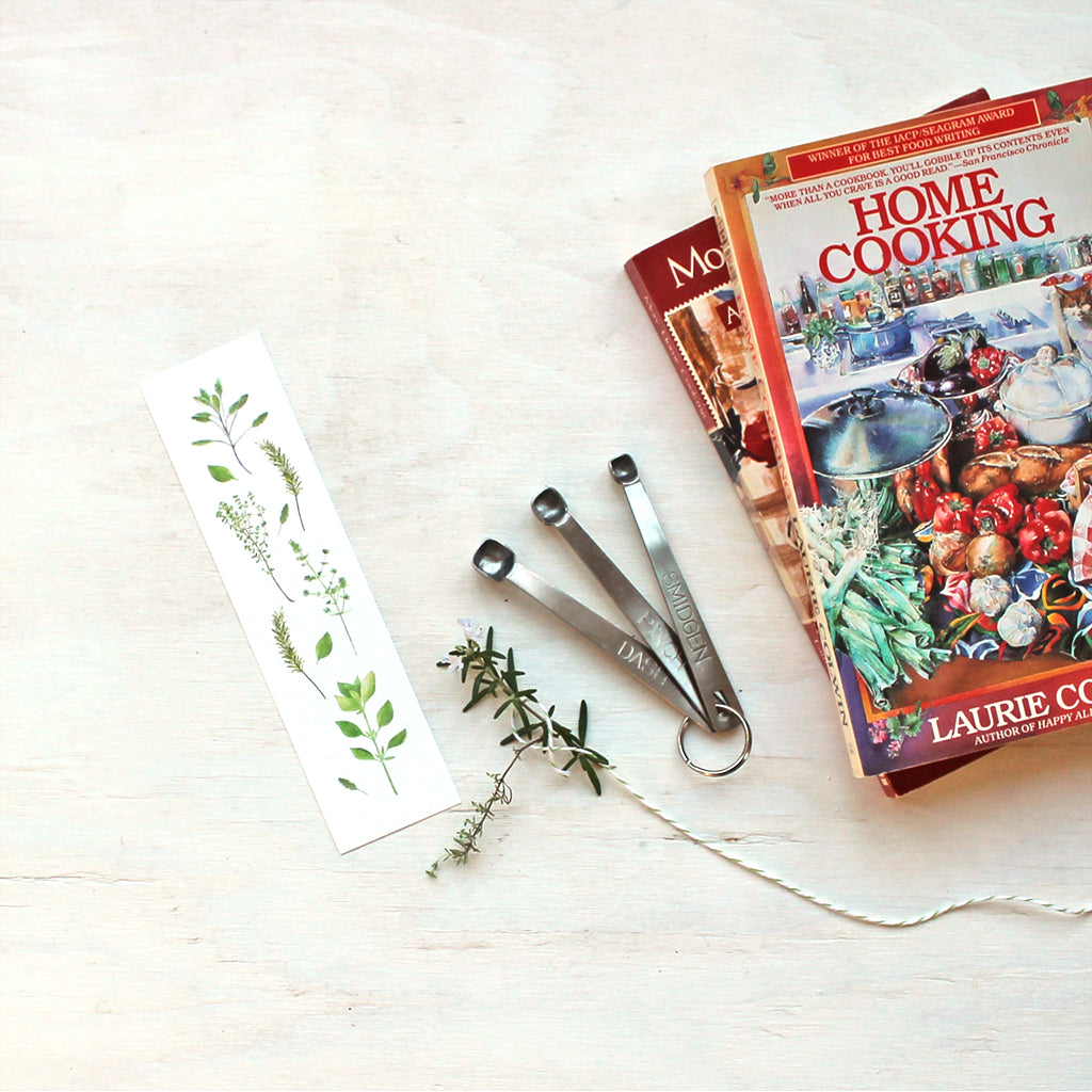 A bookmark for cookbooks featuring herbs painted in watercolor by artist Kathleen Maunder. Featuring sage, thyme, rosemary, summer savory and basil.