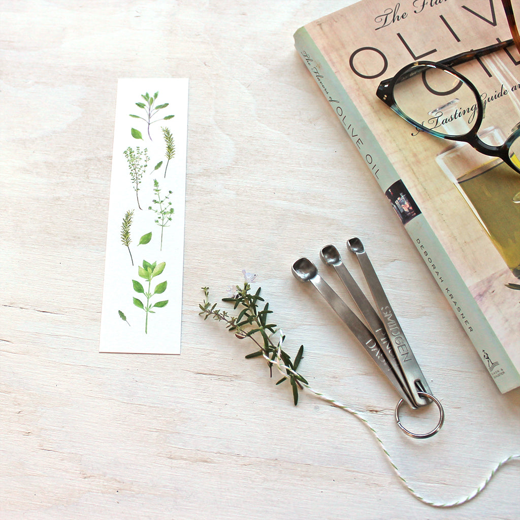 A bookmark featuring herbs painted in watercolour by artist Kathleen Maunder. Featuring sage, thyme, rosemary, summer savory and basil.