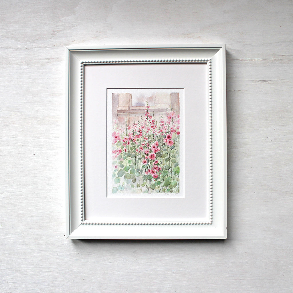 A 6 x 8 inch print of a watercolor painting of hollyhocks. Shown matted and framed. Artist Kathleen Maunder.