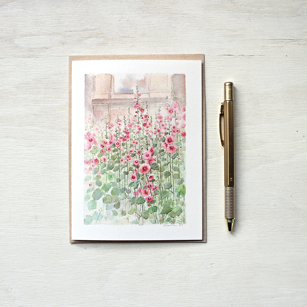 A blank note card featuring a watercolor painting of a patch of pink hollyhocks. Artist Kathleen Maunder.