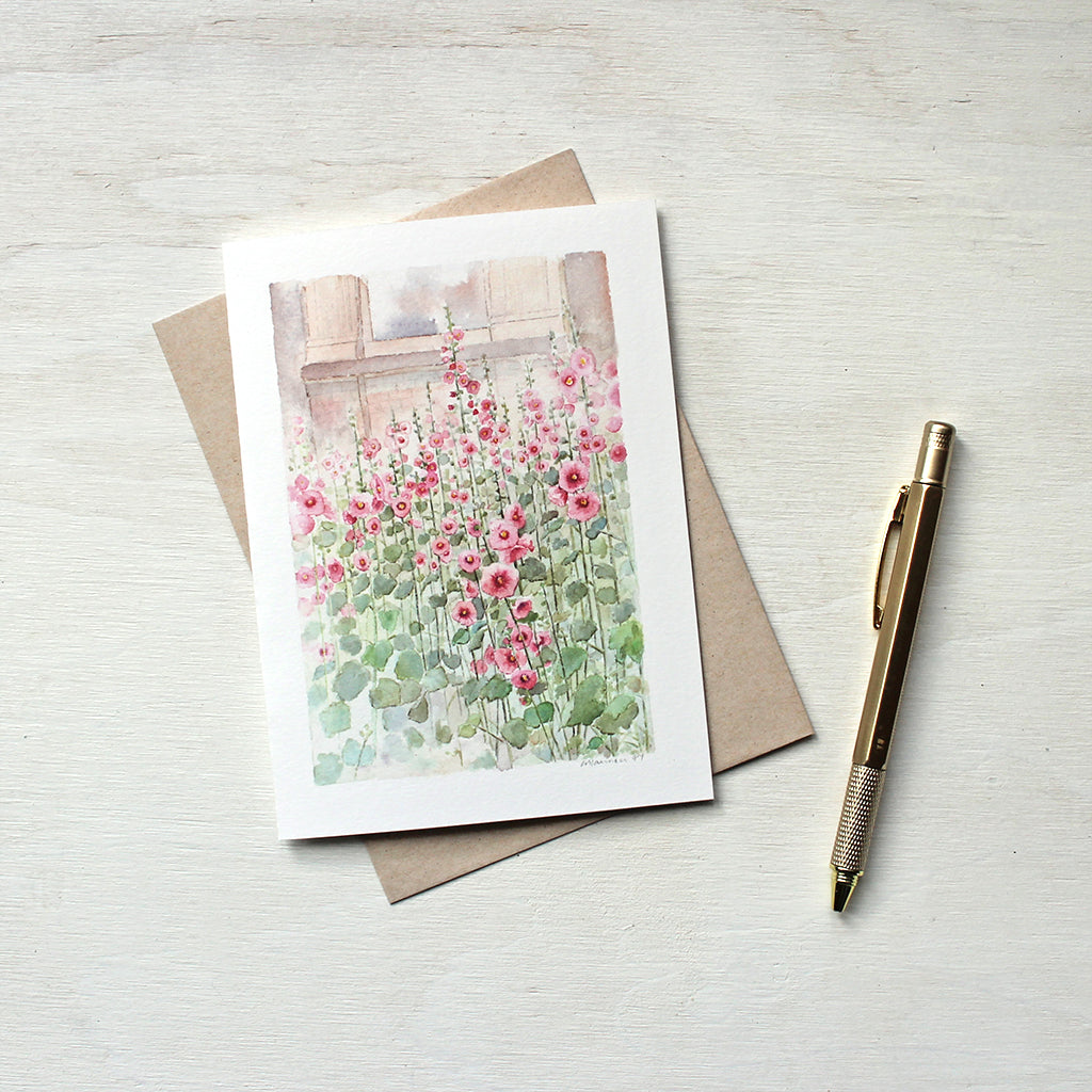 A blank notecard featuring a watercolor painting of a patch of pink hollyhocks by artist Kathleen Maunder.