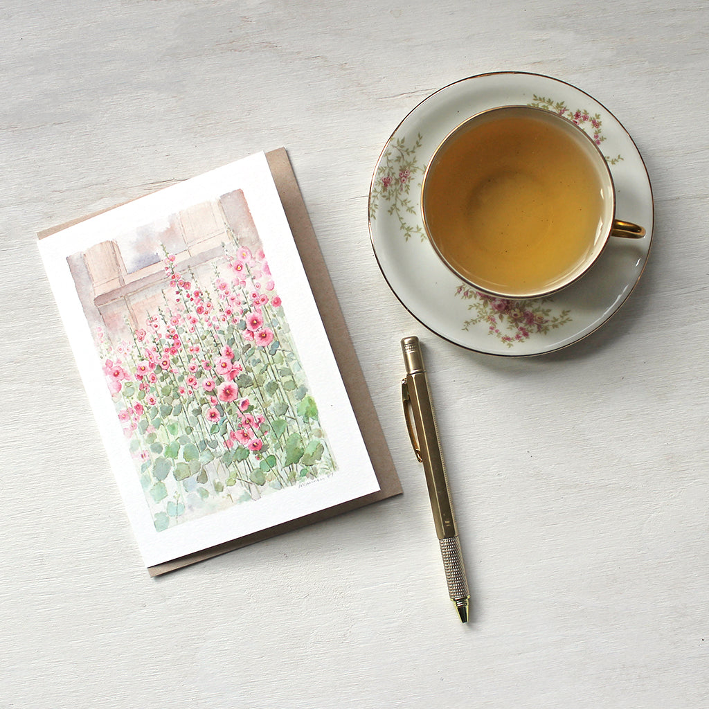 A note card featuring a watercolour painting of pink hollyhocks by artist Kathleen Maunder.