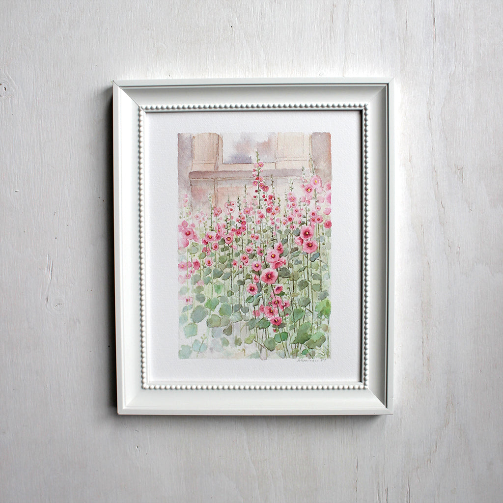 An 8 x 10 inch print of a watercolor painting of hollyhocks. Shown framed. Artist Kathleen Maunder.