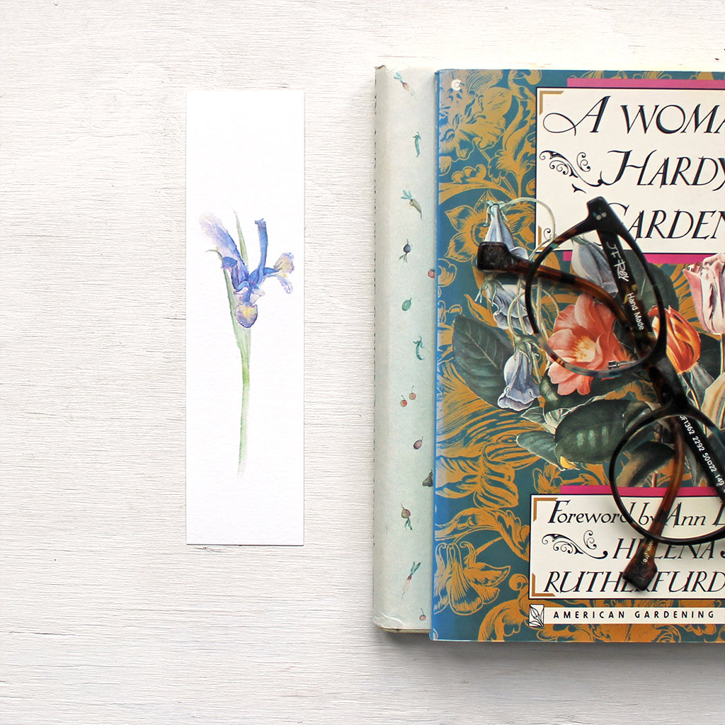 A paper bookmark featuring a painting of a blue-purple iris. Watercolor artist: Kathleen Maunder.