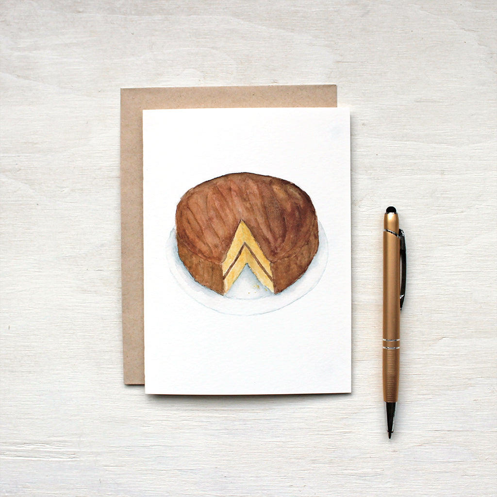 Note card featuring a watercolor painting of a vanilla and chocolate layer cake. Accompanying kraft envelope. Artist Kathleen Maunder.