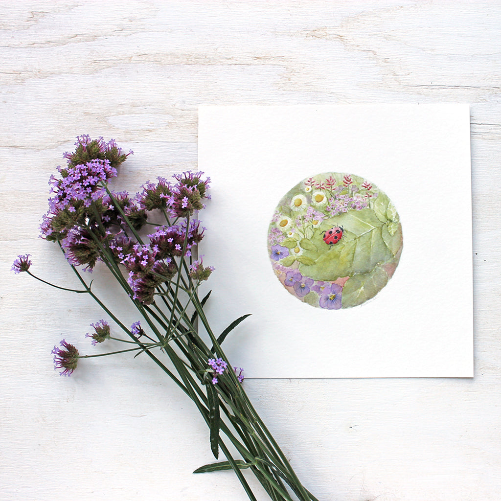 Art print featuring a delicate watercolor painting of a ladybug on a leaf surrounded by flowers. Artist Kathleen Maunder.