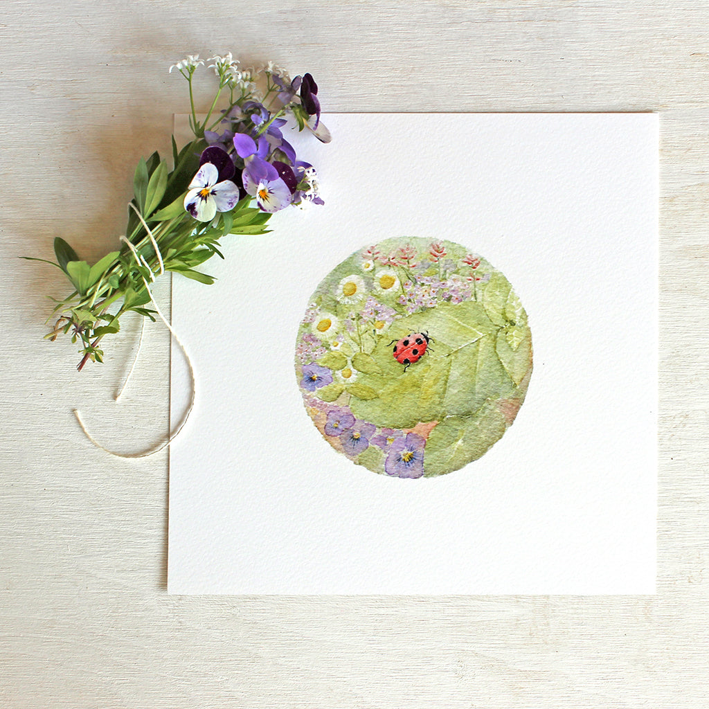 A beautiful watercolor print of a ladybug within a circle of leaves and flowers. Artist Kathleen Maunder.