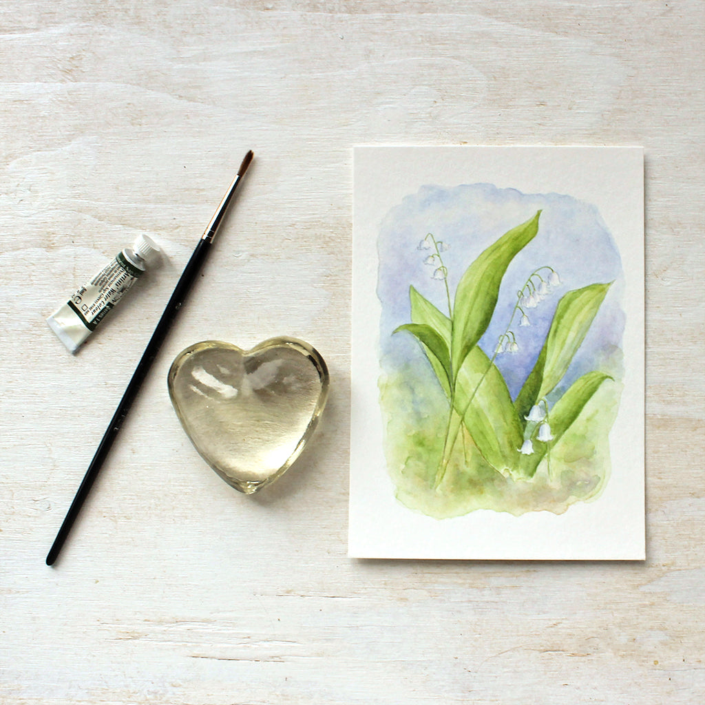 An art print of a delicate watercolor painting of lily of the valley by Kathleen Maunder. Beautiful tones of white, green and blue. 