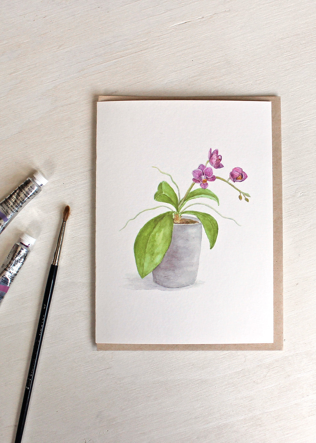 A blank note card featuring a watercolor painting of a pot of tiny purple orchids. Artist Kathleen Maunder.
