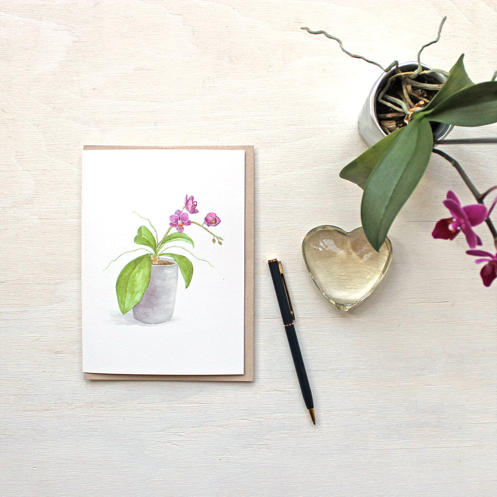 Note card featuring a watercolor painting of a pot of small purple orchids. Artist Kathleen Maunder.