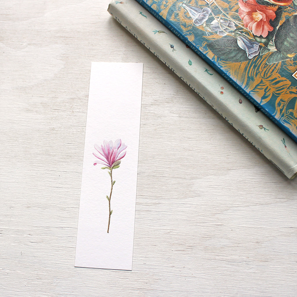 A paper bookmark featuring a pink star magnolia flower painted by watercolor artist Kathleen Maunder.