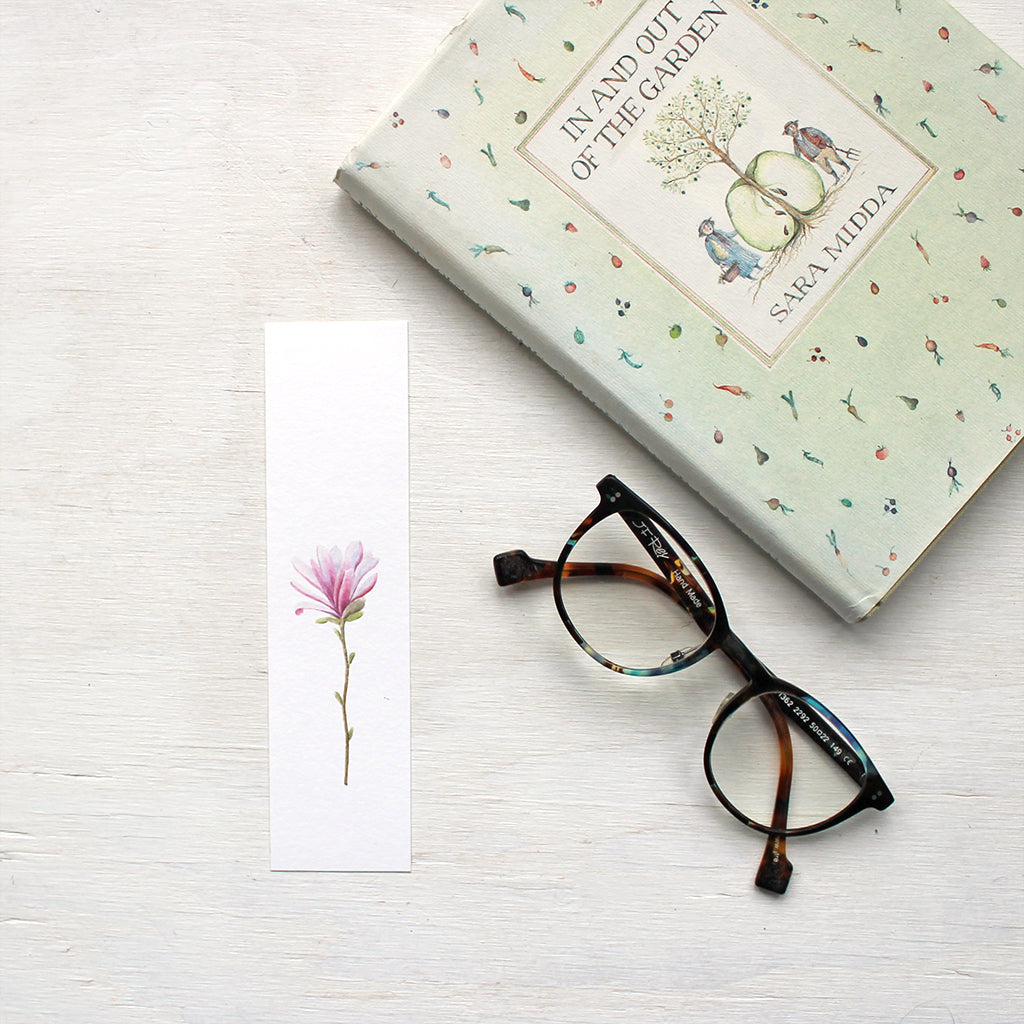 A bookmark featuring a single pink star magnolia blossom painted by watercolour artist Kathleen Maunder.