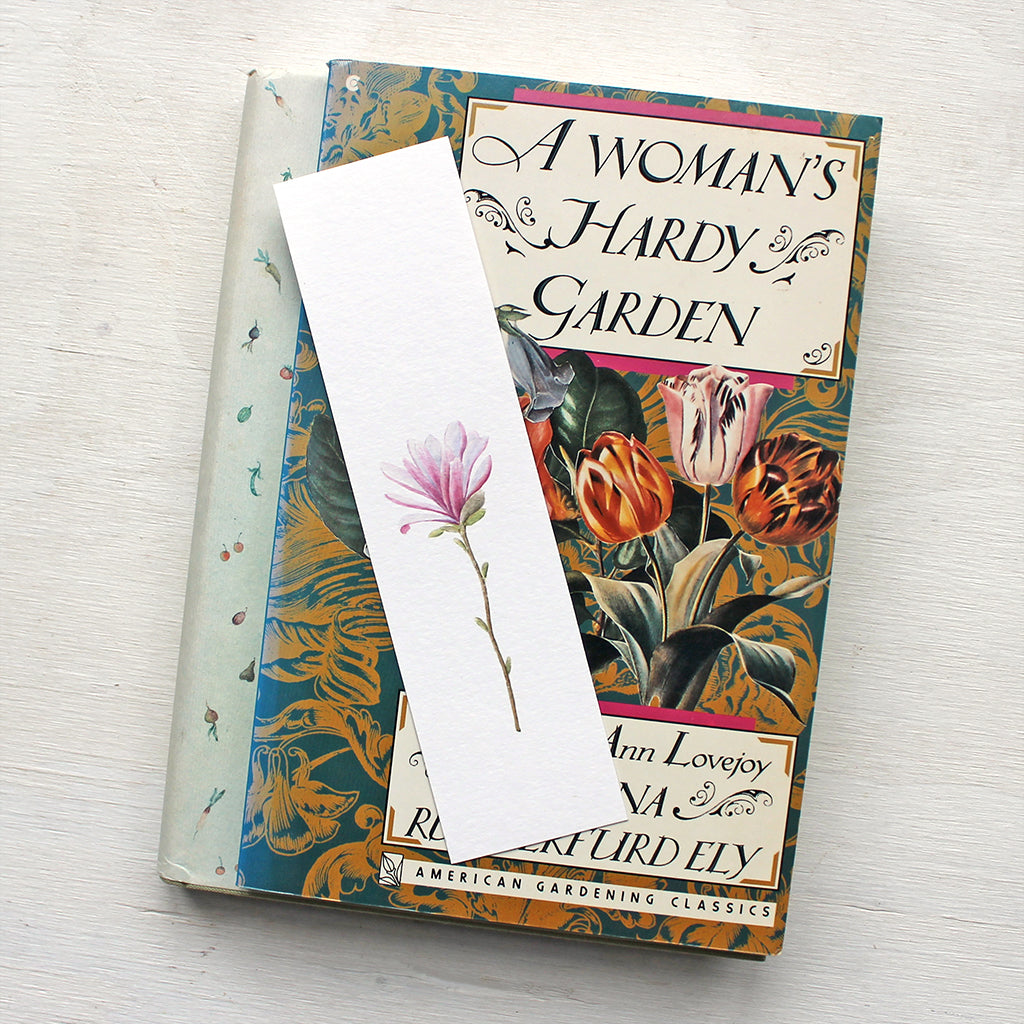 A paper bookmark featuring a pink star magnolia blossom painted by watercolor artist Kathleen Maunder.