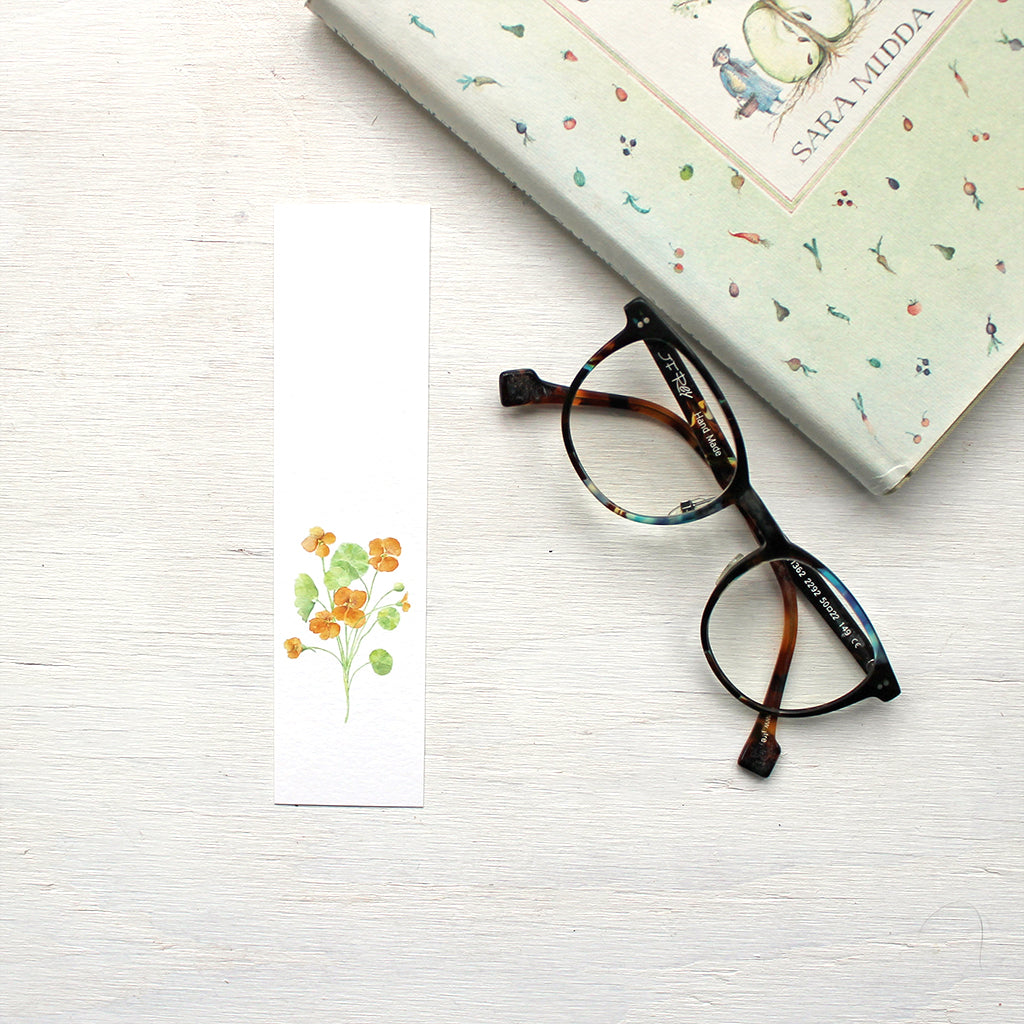 A paper bookmark featuring a watercolour painting of a stem of orange nasturtiums. Artist Kathleen Maunder.