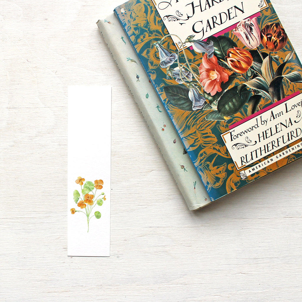 A paper bookmark featuring a watercolor painting of a stem of orange nasturtiums. Artist Kathleen Maunder.