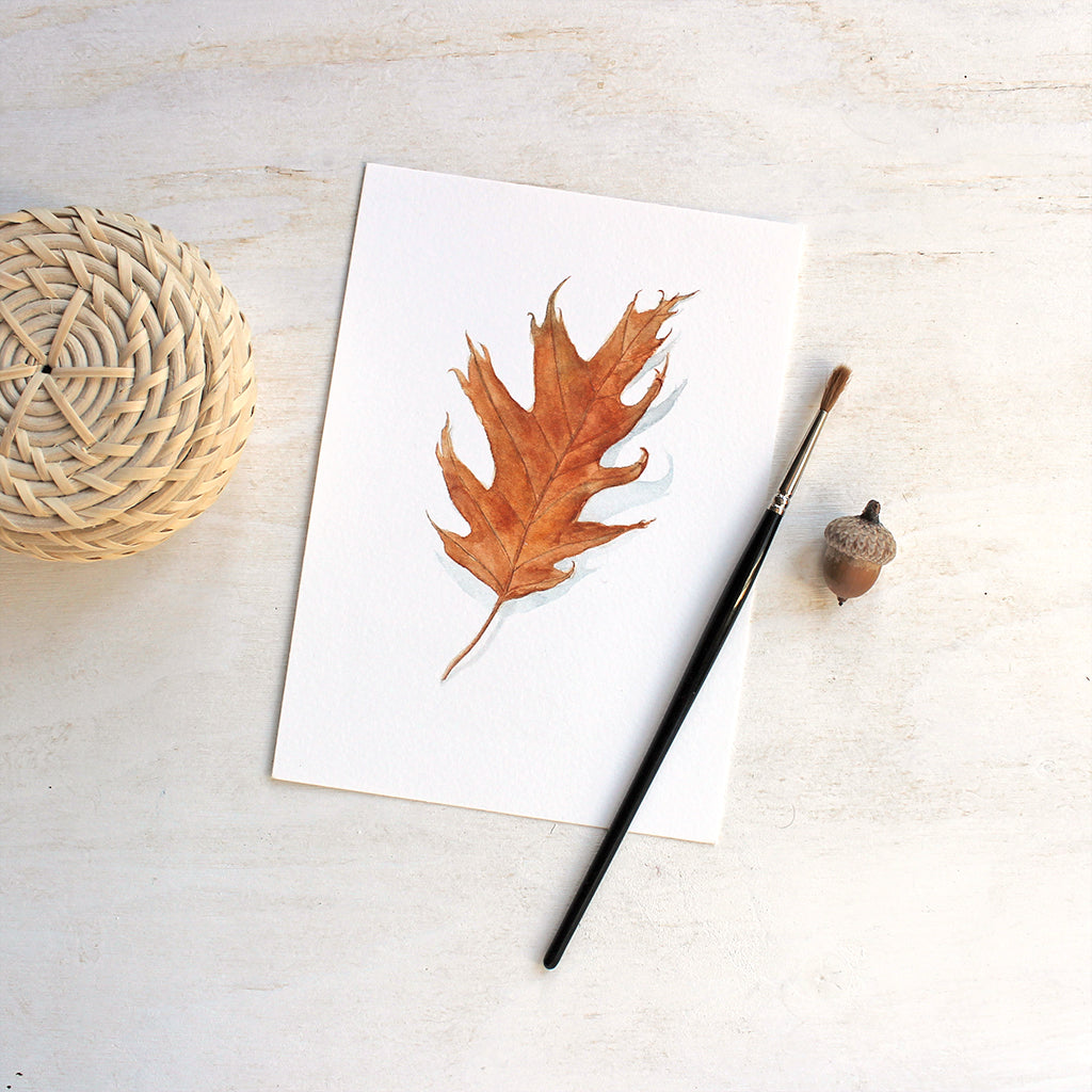 An autumn art print featuring a watercolor painting of an orange oak leaf. Artist Kathleen Maunder.