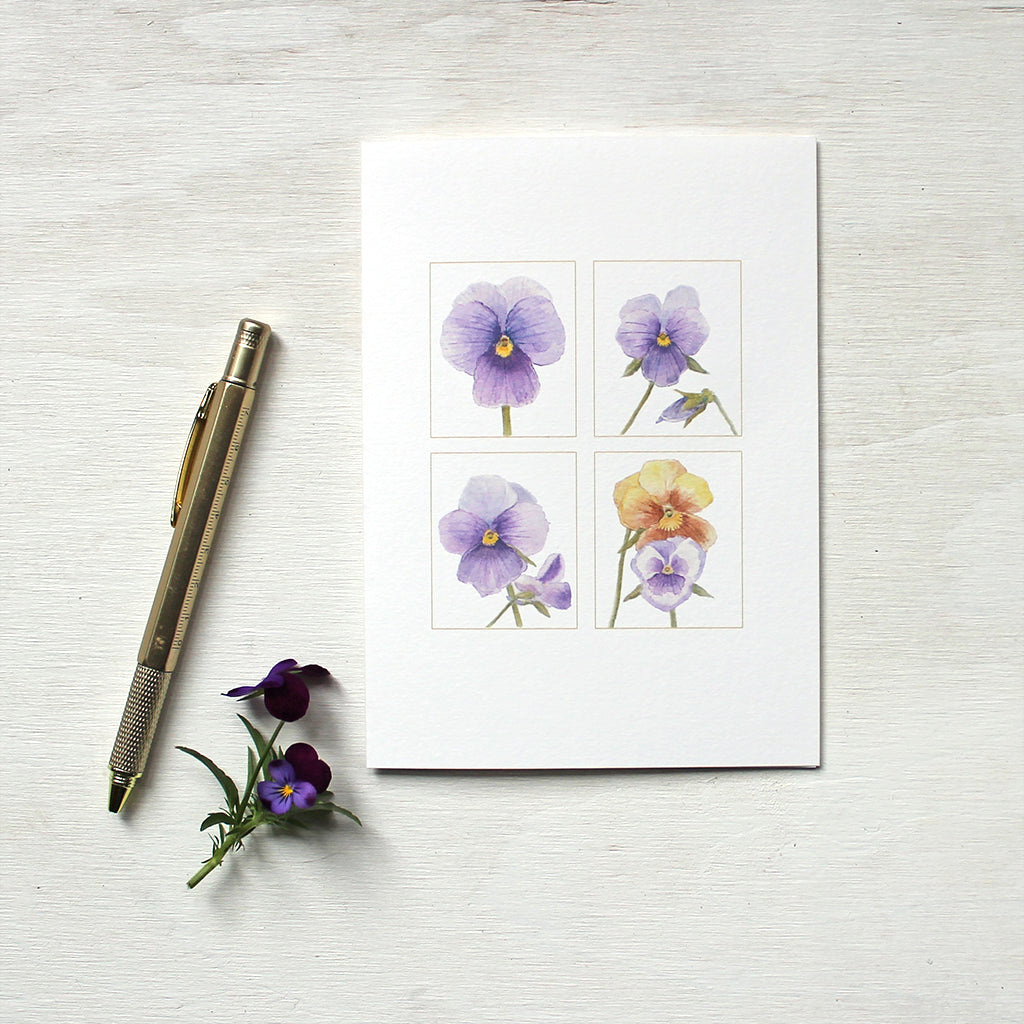 A note card featuring watercolour paintings of purple and gold pansies by artist Kathleen Maunder.