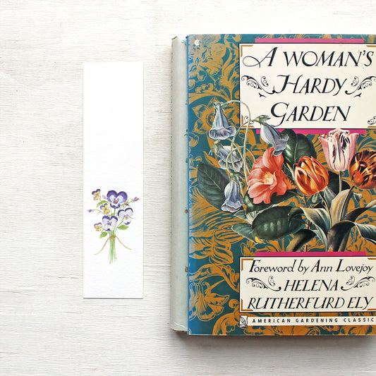 A paper bookmark featuring a watercolour painting of a tiny bouquet of purple and yellow pansies and violas. Artist Kathleen Maunder.