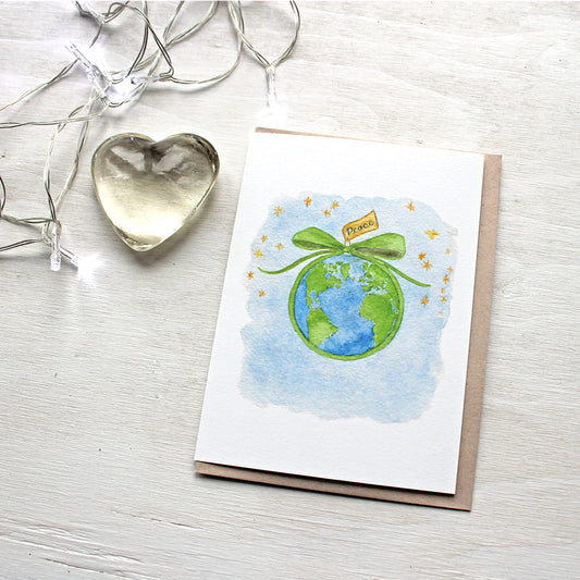 Peace on Earth holiday cards featuring the earth wrapped with a green ribbon and a peace gift tag. Artist Kathleen Maunder of Trowel and Paintbrush