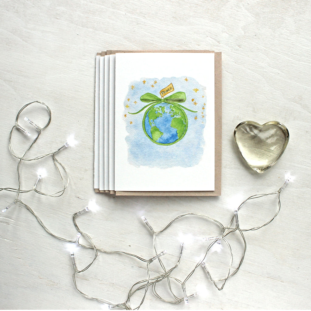 Set of Christmas cards with a watercolor painting by Kathleen Maunder of the earth tied with a green bow and a message of peace.