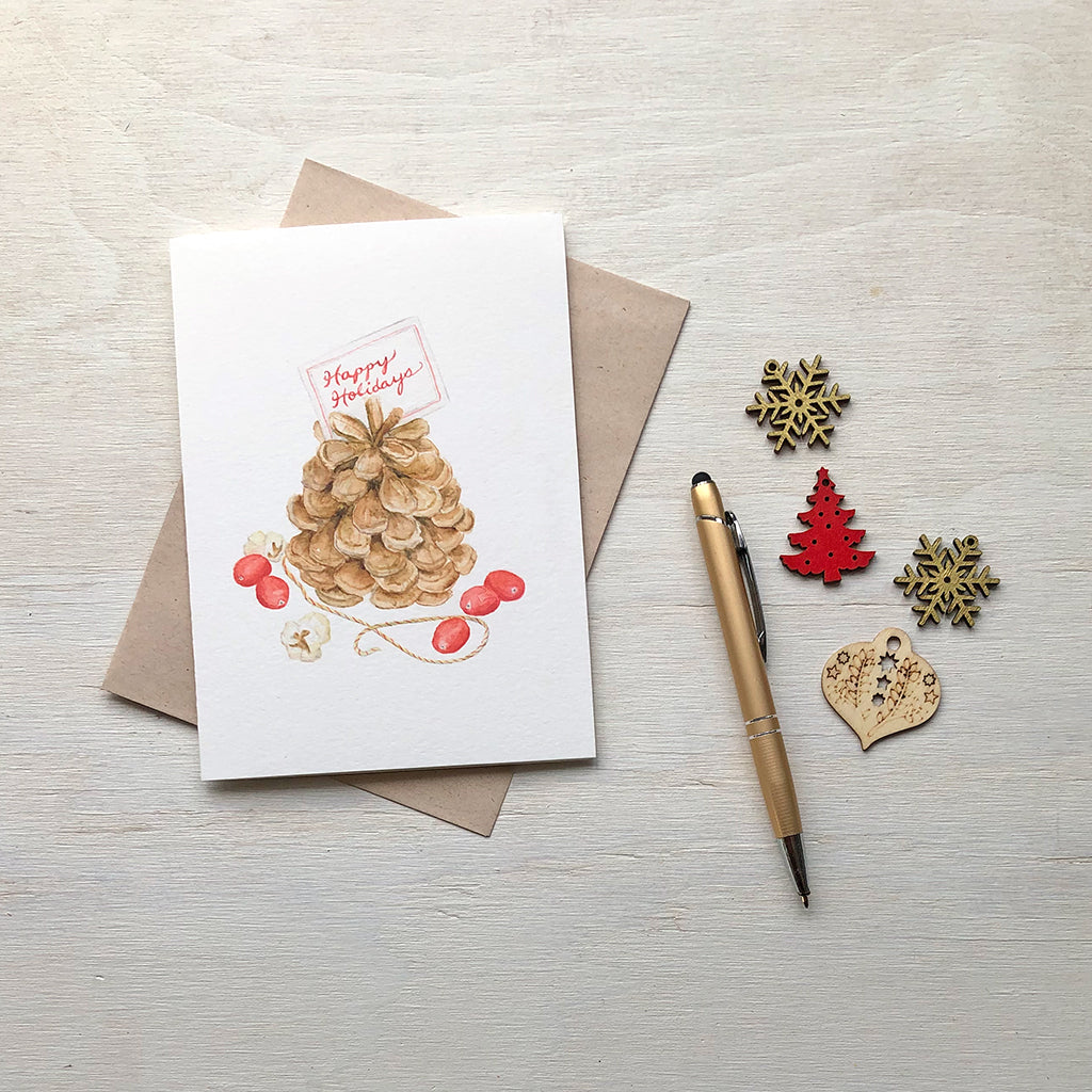 Christmas card featuring a pine cone, cranberries and popcorn. Painted in watercolor by Kathleen Maunder.