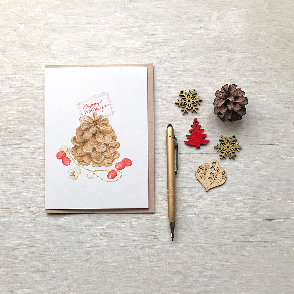 Christmas watercolour card featuring a painting of a pine cone, cranberries and popcorn. Artist Kathleen Maunder.