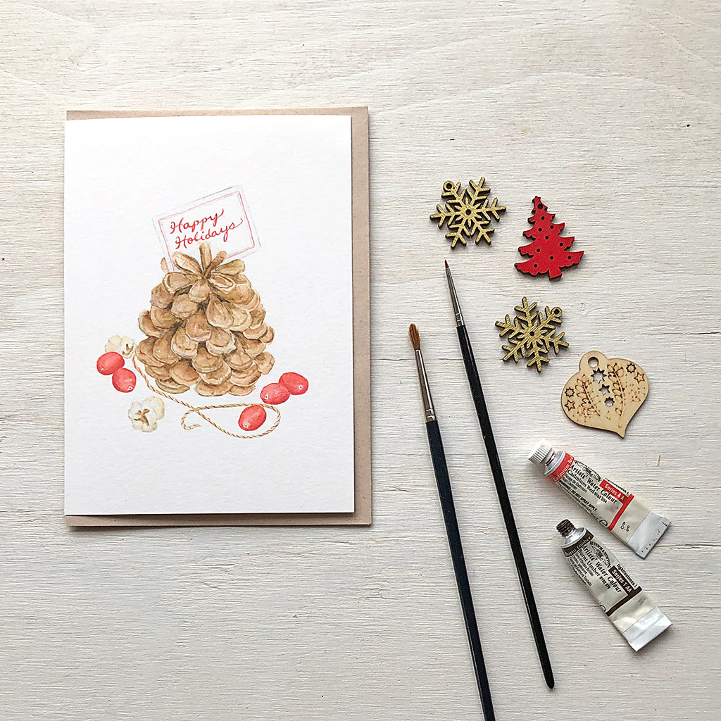 Holiday greeting card painted in watercolor featuring a pine cone, cranberries and popcorn by artist Kathleen Maunder