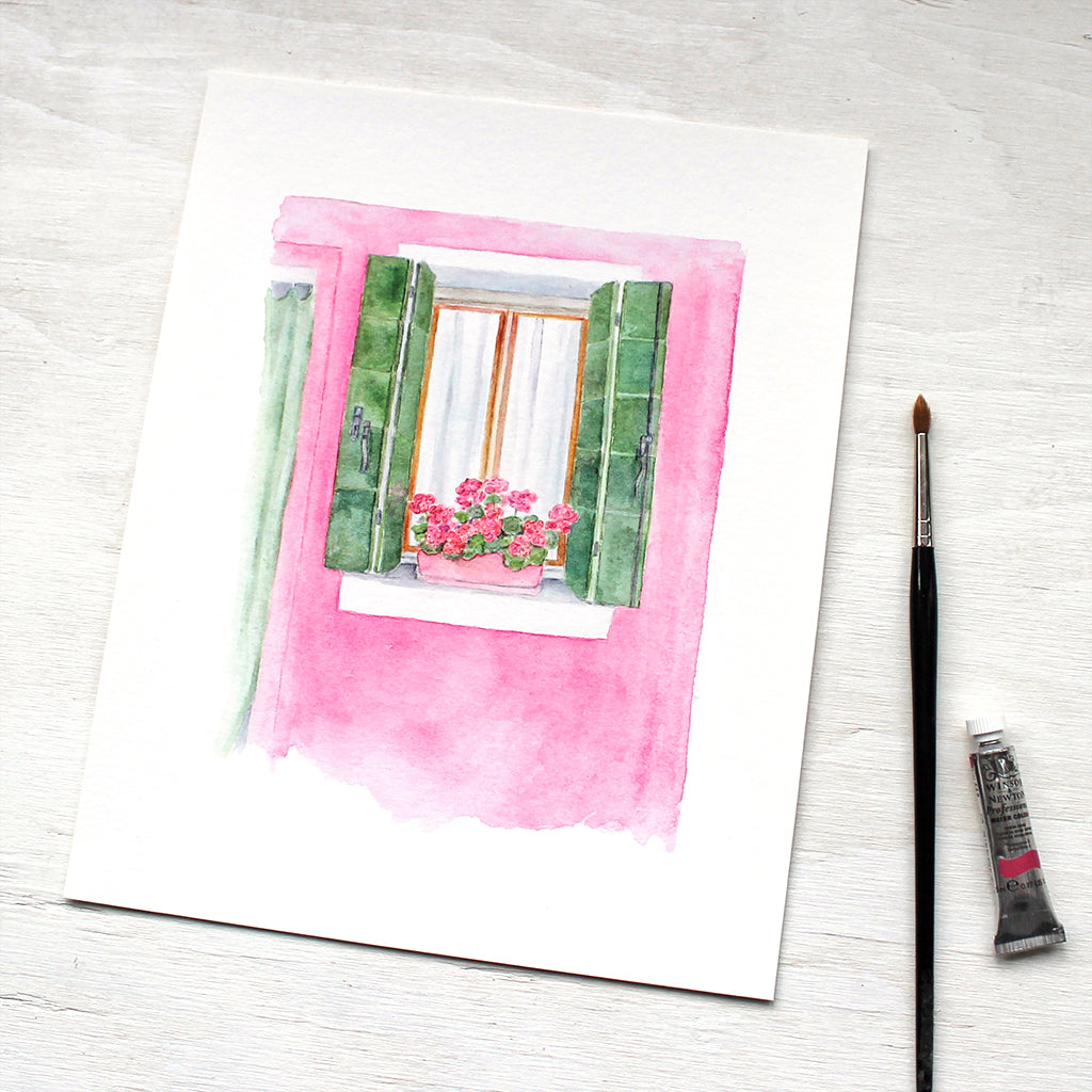 A pink house with green shutters and matching geraniums. A scene from Burano, Italy. Artist Kathleen Maunder.