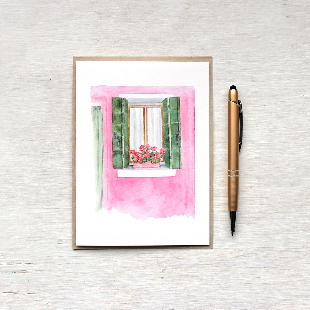A note card featuring a pink house with green shutters and matching geraniums on the windowsill. A scene from Burano, Italy. Watercolor painting by  Kathleen Maunder